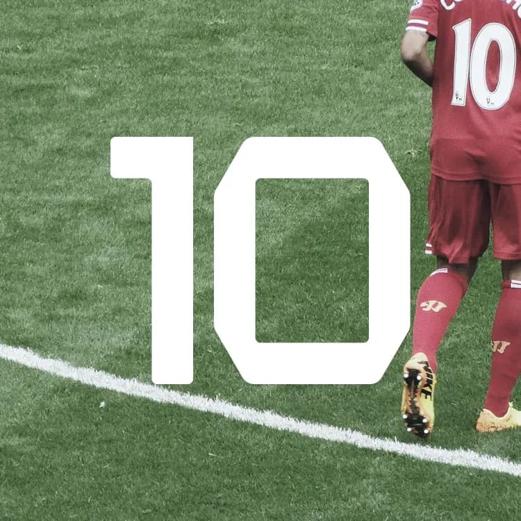 Soccer player in a red jersey with number 10 on the back, walking on a grass field near a large white number 10 marking.