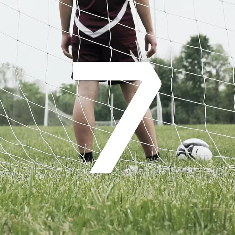 Soccer player in maroon shorts standing near a ball in front of a net, with a large white number 7 overlaying the image.