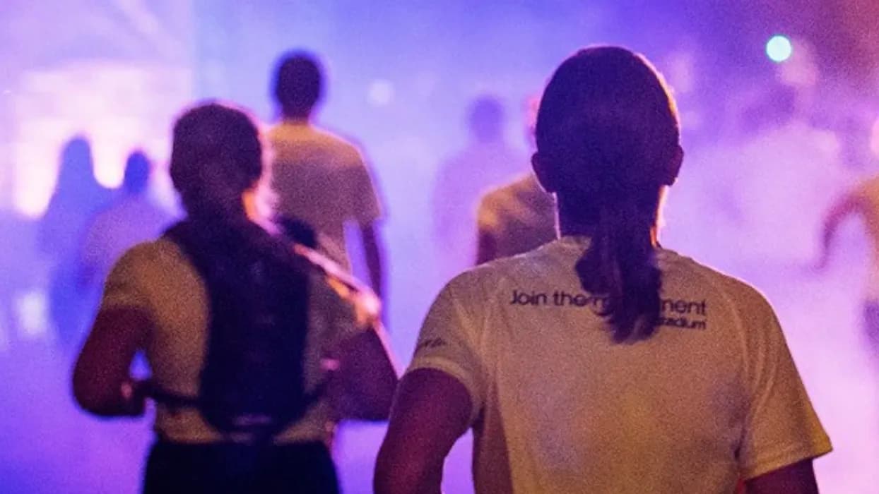 People jogging at night, illuminated by purple and blue lighting, creating a vibrant and energetic atmosphere.
