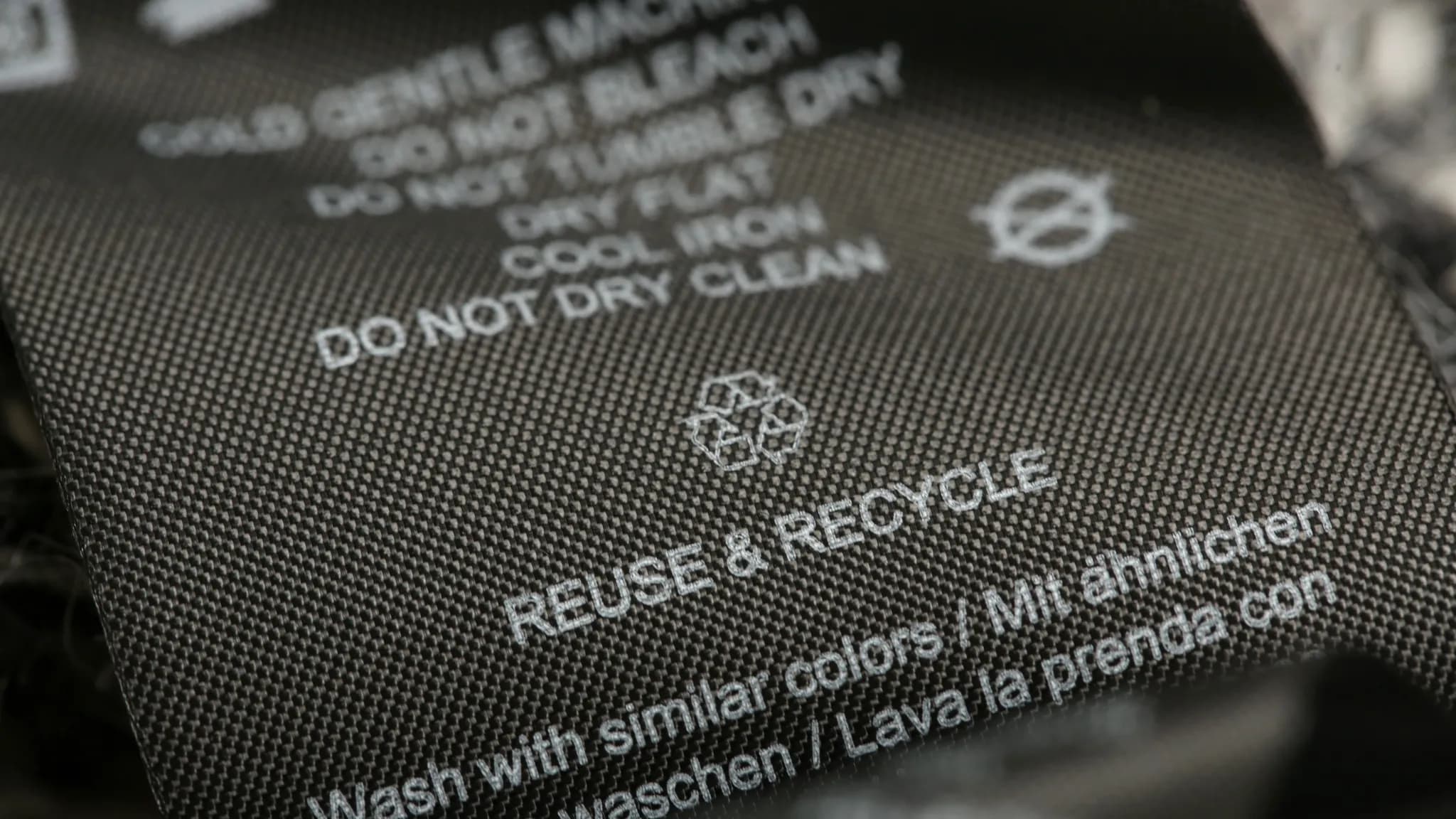 Close-up of a clothing care label with wash instructions and "Reuse & Recycle" message, featuring a recycling symbol.