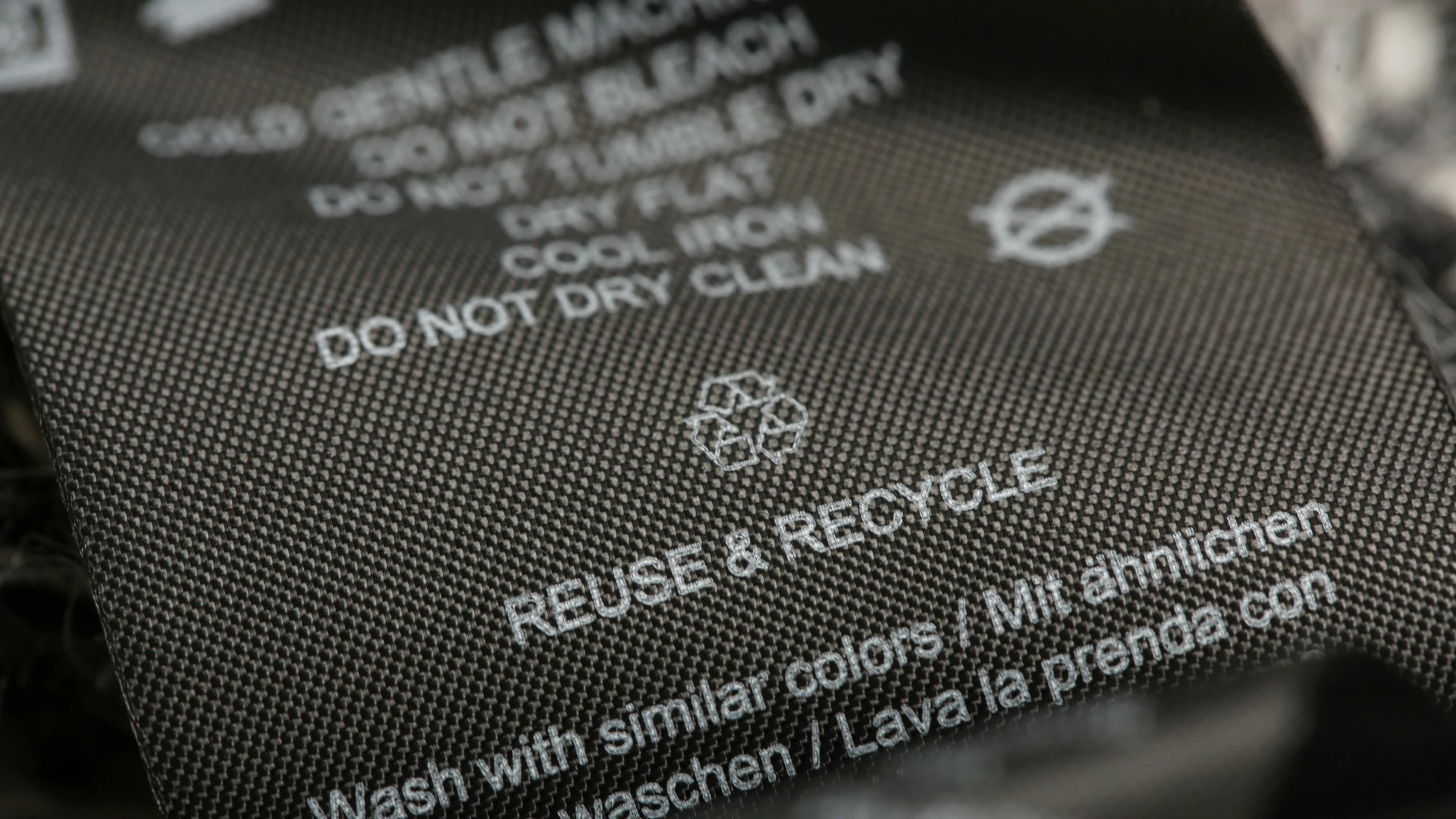 Close-up of a clothing care label with wash instructions and "Reuse & Recycle" message, featuring a recycling symbol.