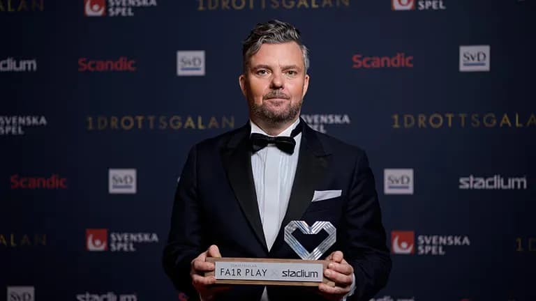 Man in a tuxedo holding a "Fair Play" award, standing against a backdrop with logos such as "Idrottsgalan" and "Svenska Spel."